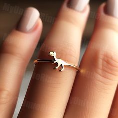 a woman's hand holding a gold ring with a small dinosaur on it