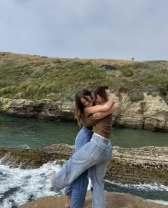 two people hugging each other while standing on rocks near the water