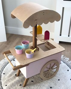 a child's wooden play table with an umbrella top and cups on the wheels