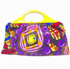 Top handle bag in the Wakanda cotton fabric that is multi colored.  Background is black with yellow, purple, pink, red, and blue throughout.  Vintage yellow marbled acrylic handles that are 13 inches wide.  Purple lining with an inside pocket in the same fabric of the bag.  Antique gold magnetic snap for closure.  Top of handles to bottom of bag 14 1/2 inches long.  Top of bag 14 1/2 inch Width Middle of bag 18 inch Width Bottom of bag 20 inch Width Multicolor Shopping Bag With Round Handle, Multicolor Shopping Bags With Round Handle, Multicolor Bags With Round Handle For Daily Use, Multicolor Bag With Round Handle For Daily Use, Daily Use Multicolor Bags With Round Handle, Multicolor Bag With Double Rolled Handles, Multicolor Shoulder Bag With Rolled Handles For Shopping, Multicolor Double Handle Bag With Rolled Handles, Multicolor Top Handle Bag With Rolled Handles