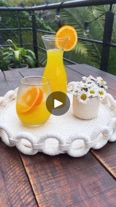 an orange juice in a glass next to two glasses on a tray with daisies