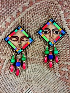 "These multi-colored diamond shaped earrings show influences of archaic  native designs. The vibrant color scheme and geometric designs are complemented with neutral facial features.  One open-eyed and the other closed eyed.  Accent beads are blue, green, red and brass. Dimensions are 2 1/8\" by 2 1/8\".  Signed by the artist." Native Designs, Diamond Shape Earrings, Native Design, Ethnic Earrings, Facial Features, Diamond Shaped, Geometric Designs, Color Scheme, Diamond Shapes