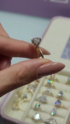 a woman's hand holding an engagement ring in front of a box of jewelry