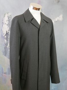 This charcoal gray overcoat is crafted from a high-quality wool-blend fabric, has a notch collar, and closes in the front with three concealed black buttons. The raglan style long sleeves feature a buttoned cuff strap, and the coat has two slanted storm pockets. The coat is lined in a black satin polyamid fabric (with one inner pocket), and a center vent in the back ensures complete ease of movement. Brand label: Oratop (Finland) Size: 44 US/UK Material: 45% Wool, 55% Polyester Condition: Near M Gray Single Breasted Long Sleeve Pea Coat, Gray Single-breasted Pea Coat, Gray Wool Coat With Lapel Collar And Button Closure, Gray Wool Coat With Lapel Collar, Gray Single-breasted Wool Coat For Fall, Gray Single-breasted Wool Coat, Solid Wool Pea Coat For Spring, Spring Wool Pea Coat, Gray Wool Coat With Button Closure