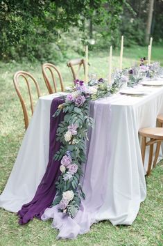 a long table with purple and white flowers is set up for an outdoor wedding reception