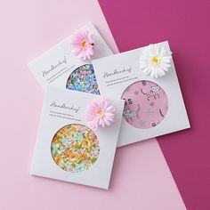 three cards with flowers on them sitting on a pink and white surface next to each other