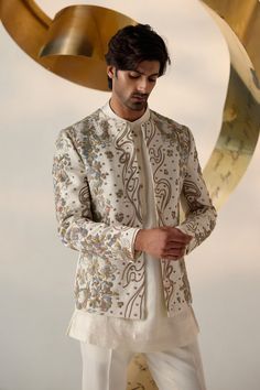 Eleven Eleven Short Jacket | Jatin Malik Introducing our renowned Short Jacket silhouette in a sophisticated dirty ivory color. This exquisite piece is hand-embroidered with colorful resham threads, gold zari, dabka, and twisted line details, creating a vibrant and intricate design. Paired with a short-length kurta featuring potli buttons and tapered trousers, this ensemble perfectly balances traditional craftsmanship with modern elegance. Ideal for making a standout impression at any special occasion, this outfit showcases our commitment to impeccable style and refined artistry. Included in purchase: Short Jacket, Kurta, Trousers Product Specification Color: Ivory Fabric: Linen Silk Occasion: Engagement, Wedding, Bridal, Reception Style: Short Jacket, Kurta, Trousers Care: Dry Clean Work: Indian Men Wedding Outfit Groom Attire, Nawabi Style Men, Men In Traditional, Engagement Dress For Men, Jatin Malik, Potli Button, Indian Wedding Suits Men, Jacket Silhouette, Wedding Kurta For Men