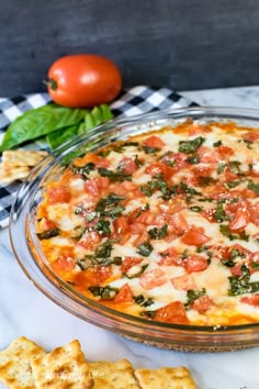 a pizza sitting on top of a glass pan covered in cheese and toppings next to crackers