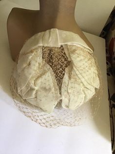 "Vintagw 1950's 1960's Off White hat with veiling. Has an Off White Velvet bow in the back. *MORE INFORMATION BELOW* CONDITION: I note a hole in the veiling on the left side (SEE PIX). Also a split in the veiling on the right side (SEE PIX). Sold As Is! MEASURES: Left to right UP and OVER the hat~12\" Front to back~7\" *WE APOLOGIZE~BUT WE NO LONGER SHIP TO GERMANY, ITALY OR SPAIN. IF ORDERS COME IN FROM GERMANY, ITALY OR SPAIN, WE WILL HAVE TO CANCEL THEM AND REFUND YOUR MONEY. SORRY FOR THIS I Vintage Cloche Headpieces For Evening, Vintage Cream Hat For Evening, Vintage White Fascinator For Evening, Vintage White Evening Fascinator, Vintage Fitted Cream Fascinator, Vintage Cloche Fascinator For Wedding, White Vintage Cloche Fascinator, Vintage Beige Fascinator For Evening, Vintage Cloche Wedding Headpiece