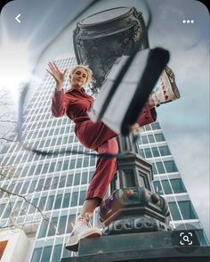 a woman standing on top of a lamp post in front of a tall building