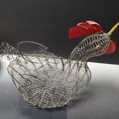 a wire sculpture of a chicken with a red beak and tail, sitting on a table