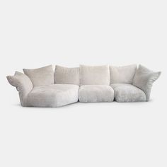 a large white couch with pillows on the top and bottom corner, in front of a gray background