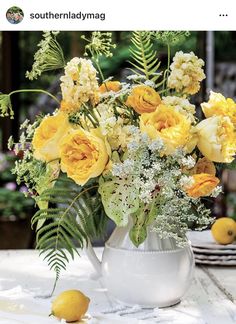 a white pitcher filled with yellow flowers sitting on top of a table next to lemons