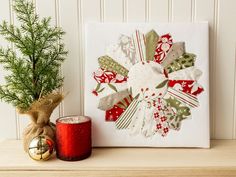 a small christmas decoration next to a candle on a mantle with a holiday ornament