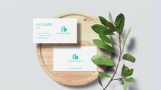 two business cards sitting on top of a wooden plate next to a leafy branch