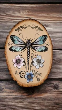 a dragonfly painted on top of a piece of wood with flowers and leaves around it