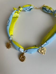 a blue and yellow necklace with gold charms on the clasp, sitting on a white surface