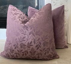 two purple pillows sitting on top of a wooden floor next to a fire place with a fireplace in the background