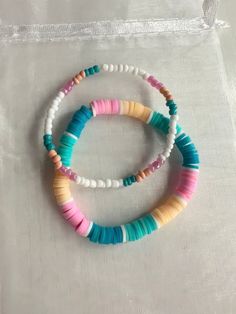 two bracelets with different colored beads sitting on top of a white cloth covered bag