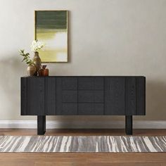 a black sideboard sitting on top of a hard wood floor next to a painting