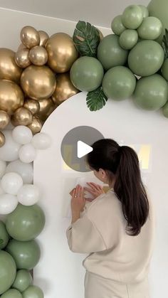 a woman standing in front of a wall with balloons and greenery on the walls