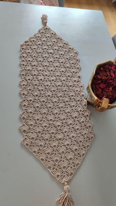 a crocheted table runner with tassels and a bowl of dried flowers