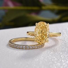 a fancy yellow diamond ring set on top of a white surface with flowers in the background