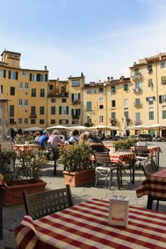 an outdoor dining area with tables, chairs and umbrellas in front of yellow buildings