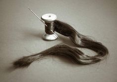 a spool of thread next to a piece of hair on a white surface with a needle sticking out of it