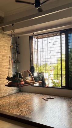 a man sitting on a swing in the middle of a room with a large window