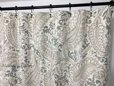 a white and gray curtain hanging from a metal rod in front of a window with an ornate pattern on it