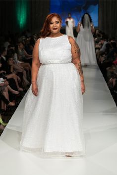 a woman in a white dress walking down a runway