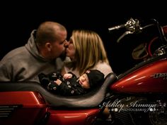 a man and woman kiss as they sit on a motorcycle with a baby in the seat