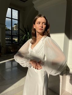 a woman standing in front of a window wearing a long white dress with sheer sleeves