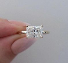 a person is holding an engagement ring with a princess cut diamond in it's center