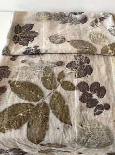 an old blanket with leaves on it sitting on a white tablecloth covered in brown and green fabric