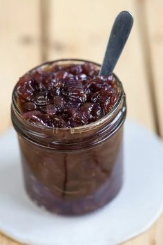 a jar filled with jelly sitting on top of a white plate next to a spoon