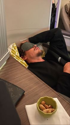 a man laying in bed with his eyes closed next to a bowl of food on the table