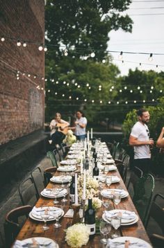 a long table with plates and silverware is set for an outdoor dinner in the backyard