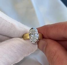 a person holding a diamond ring on top of a white cloth covered napkin with a gold band