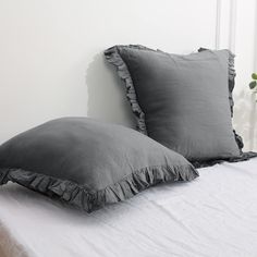 two gray pillows sitting on top of a white bed next to a potted plant