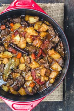 a red pot filled with stew on top of a wooden table next to a cloth