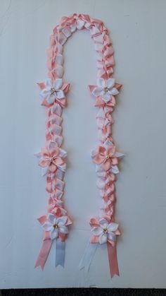 a pink and white necklace with bows on it's sides, attached to a wall