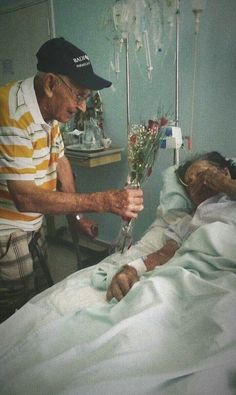 an old man in a hospital bed with flowers on his hand and another person laying down next to him