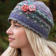 a woman wearing a knitted hat with flowers on the front and side, looking to her left