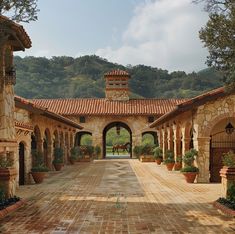 an outdoor courtyard with arches and potted plants on either side, surrounded by mountains