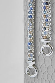 two silver bracelets with blue and white beads hanging on a wall next to each other