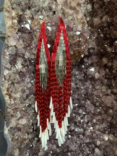 two red and white beaded earrings sitting on some rocks