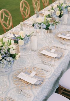 the table is set with white and blue flowers in vases, napkins, and place settings