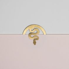 a gold brooch sitting on top of a pink box with a snake in the middle